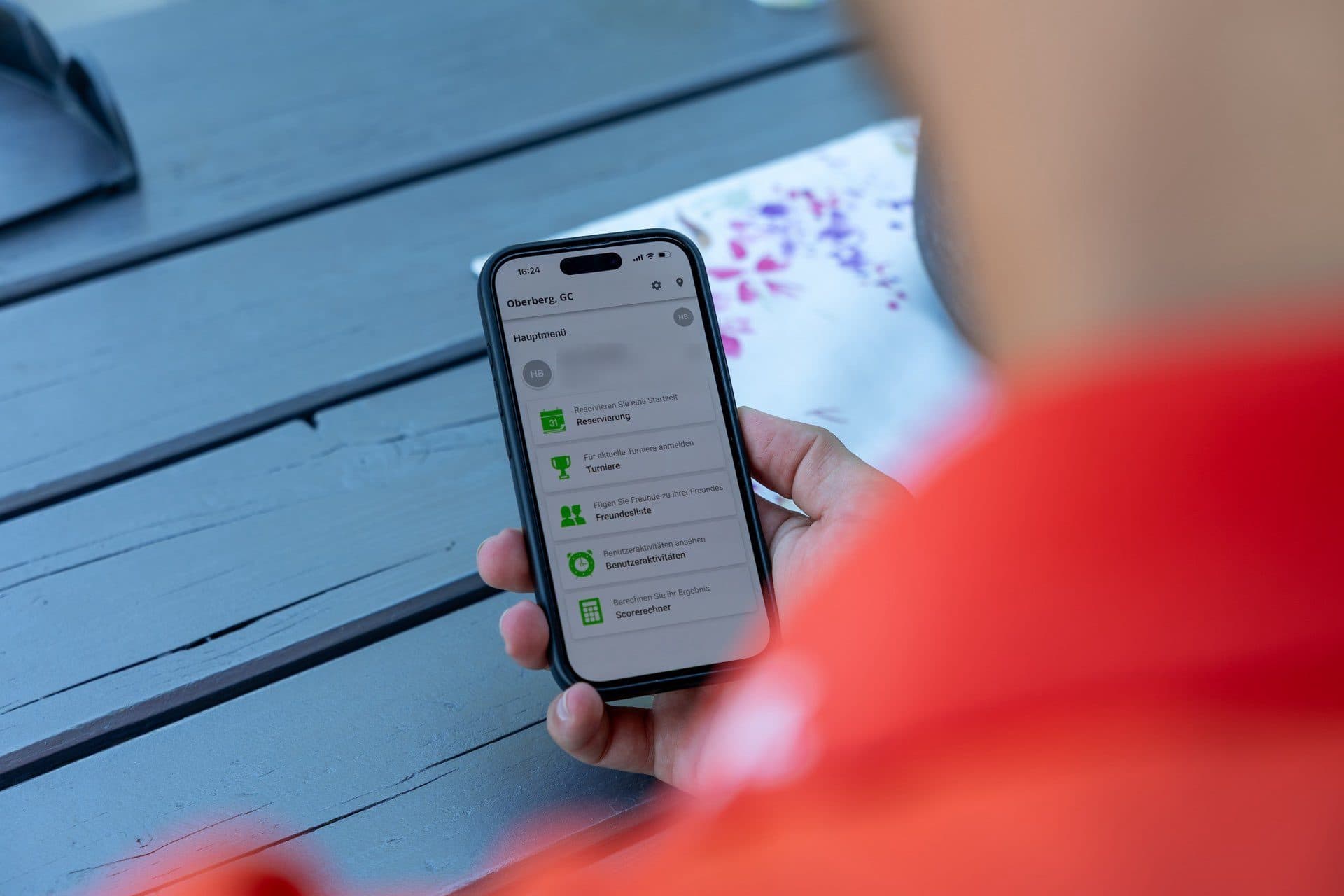 Hand hält ein Smartphone mit geöffneter Club-App und Buchungsmenü