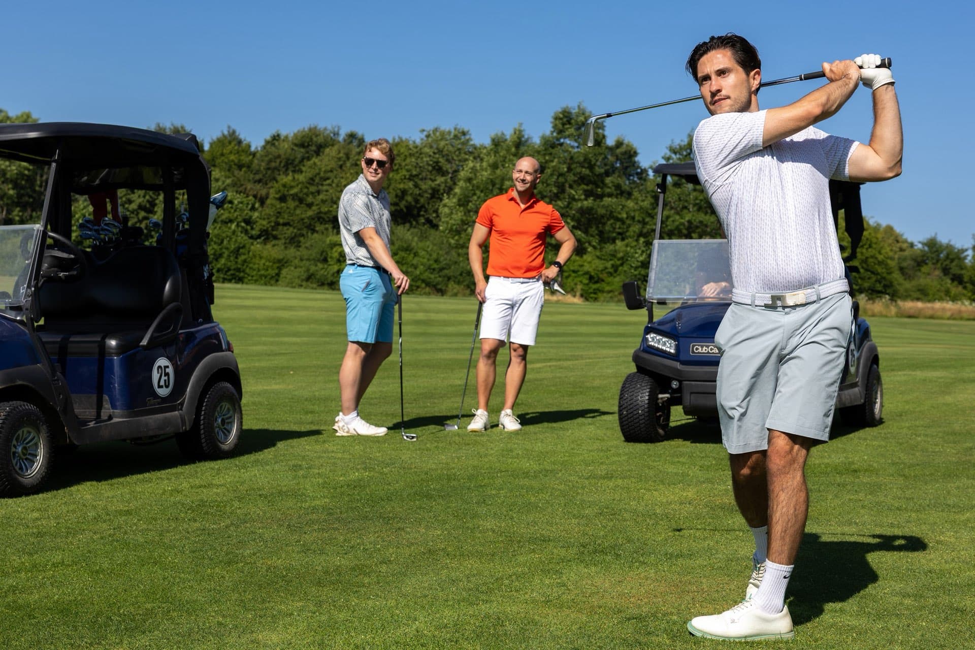Drei Spieler mit zwei Golfcarts auf dem Fairway, einer im Finish