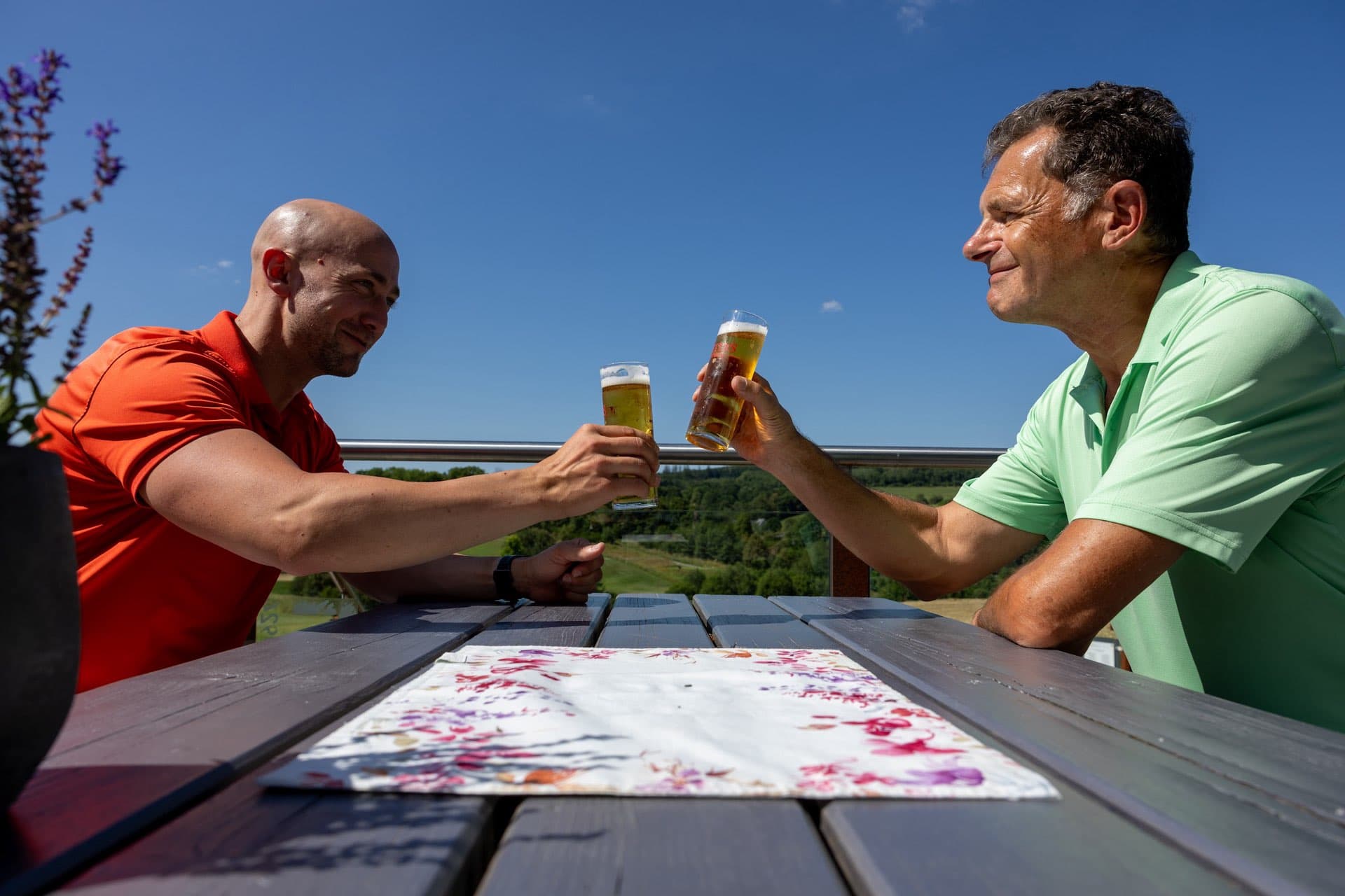Zwei Mitglieder stoßen mit Biergläsern auf der Terrasse an