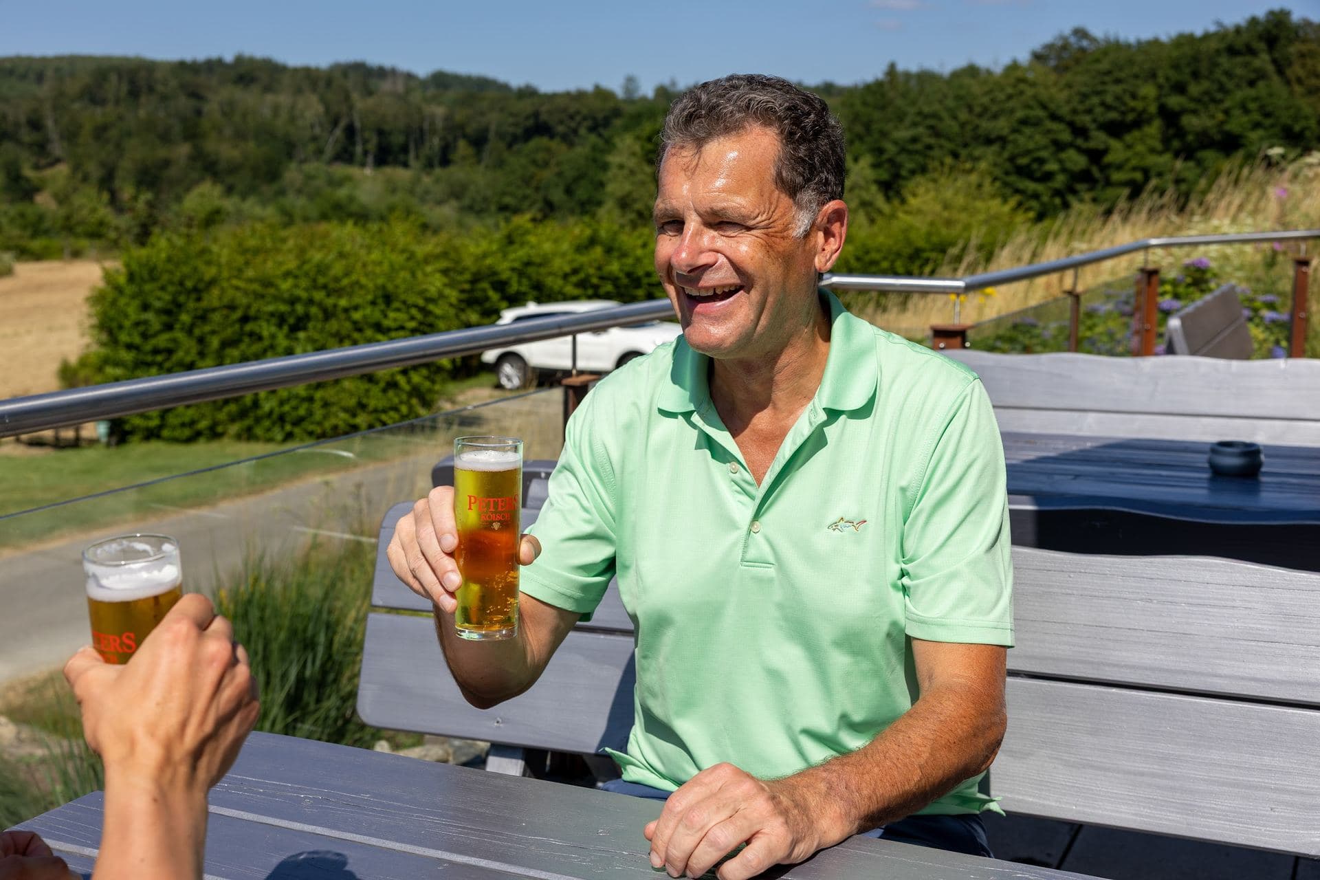 Mitglied mit einem frisch gezapften Bier auf der Terrasse