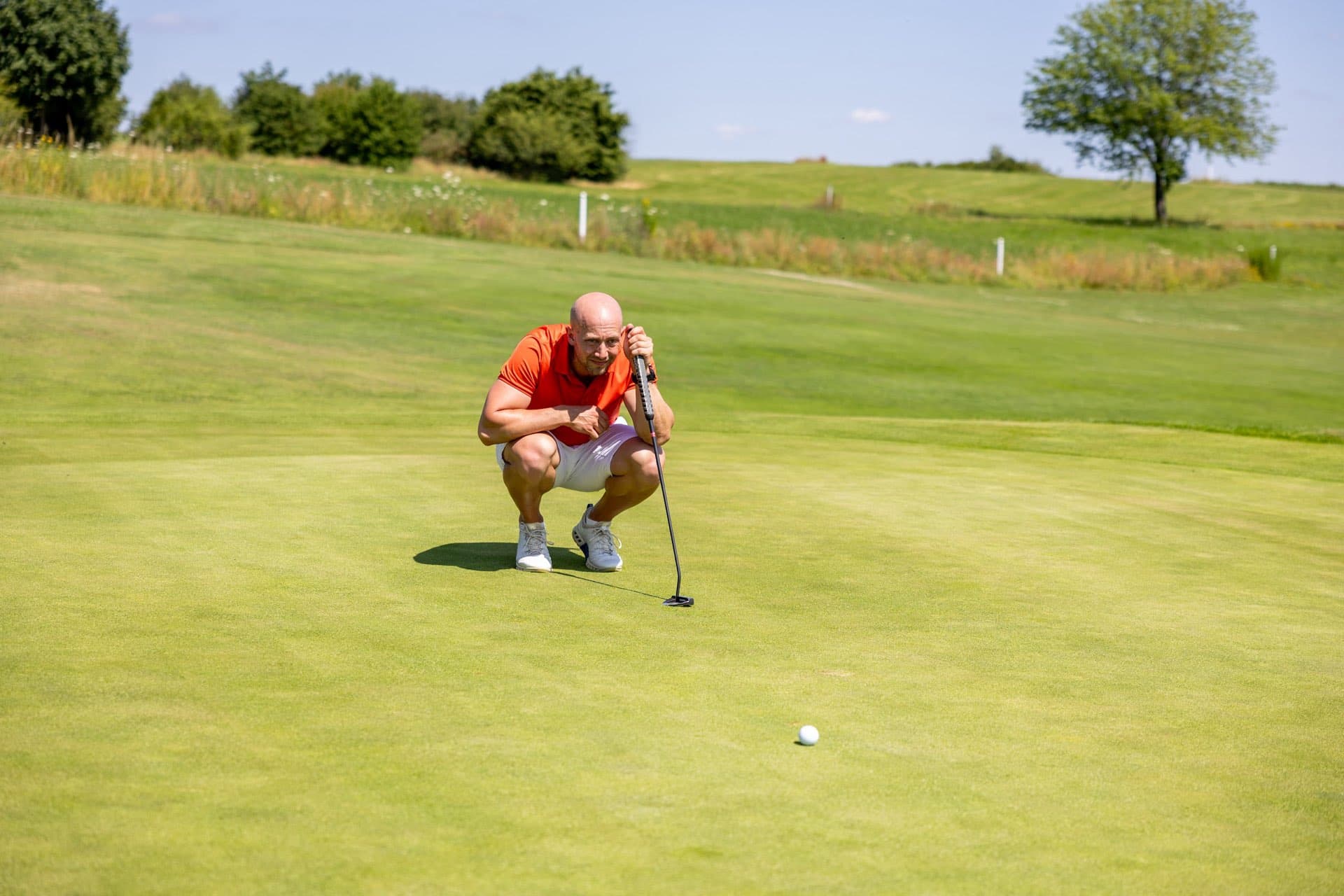 Golfer hockt auf dem Grün und liest die Puttlinie