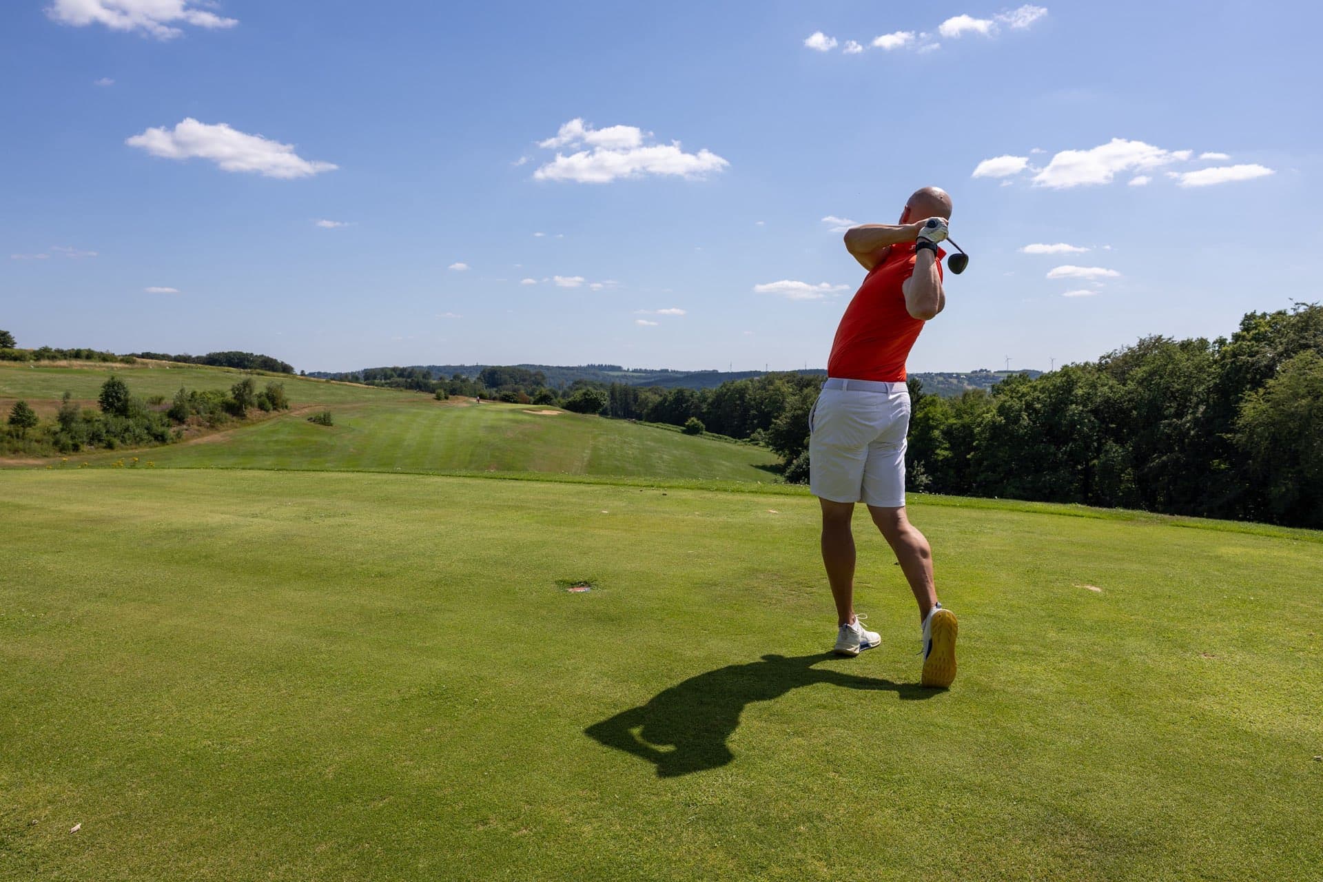 Golfer im Finish auf erhöhtem Abschlag über dem weiten Fairway