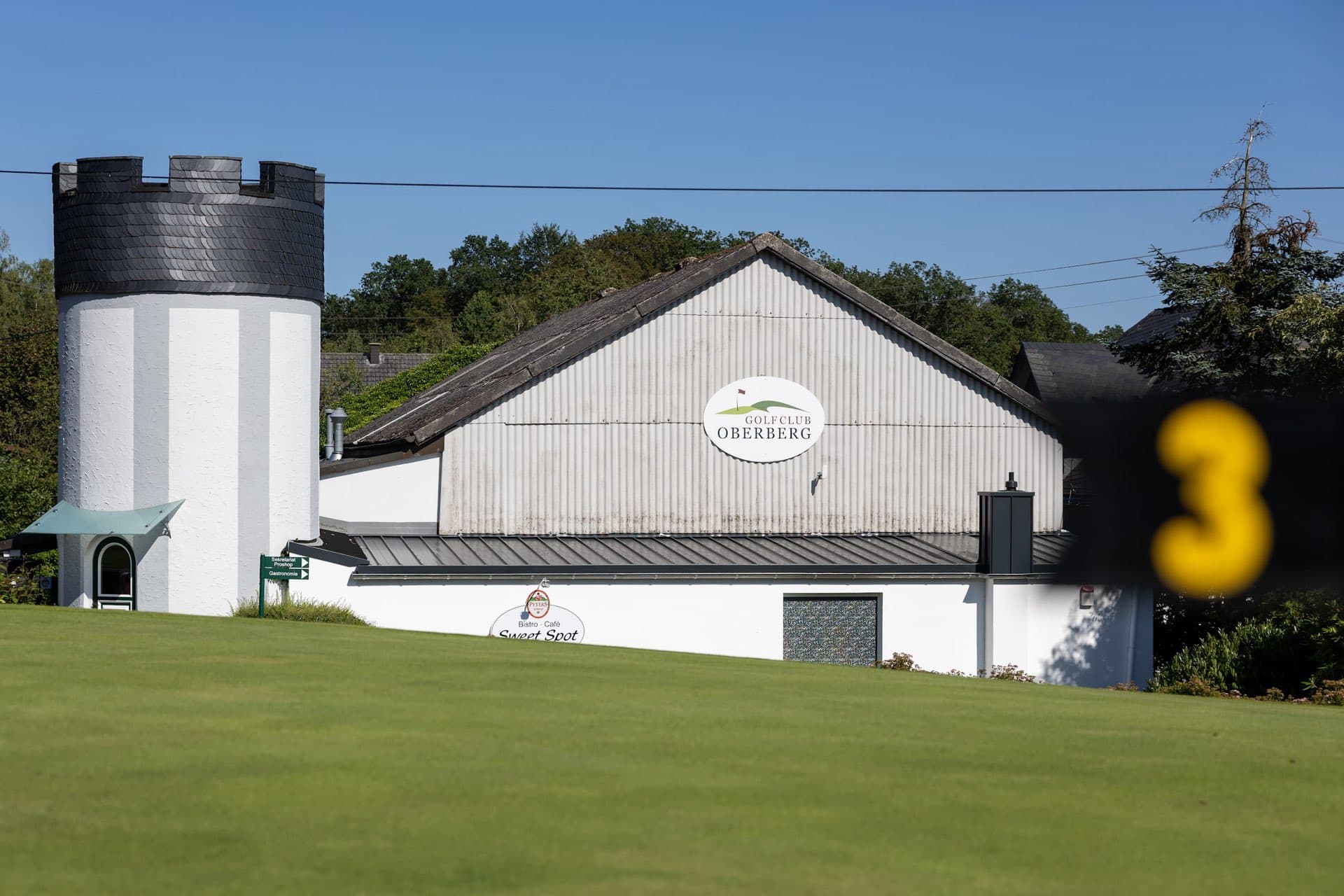 Clubhaus des Golf Club Oberberg mit Turm und Schild Sweet Spot